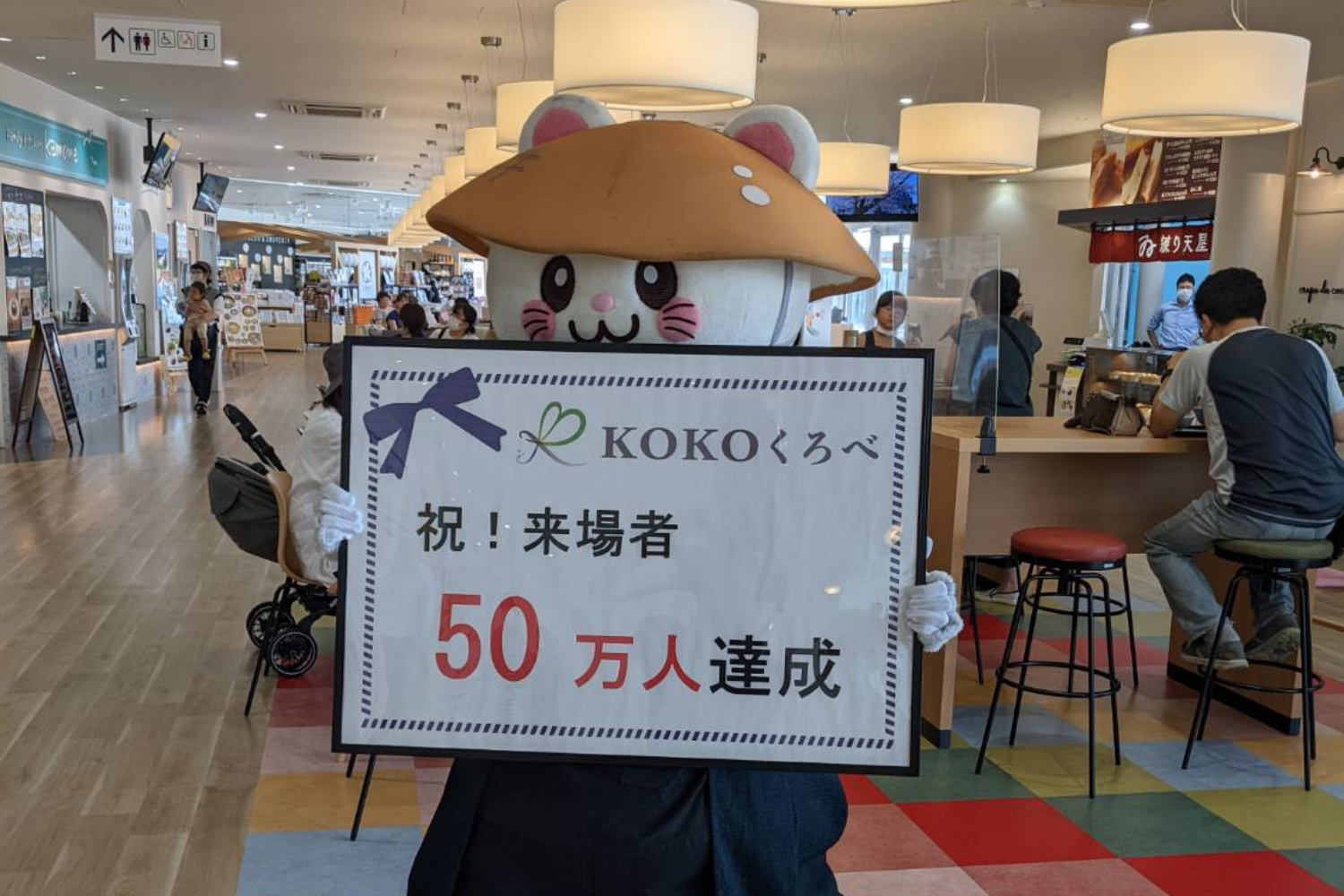 「KOKOくろべ 祝!来場者50万人達成」の札を持つばいにゃこさん