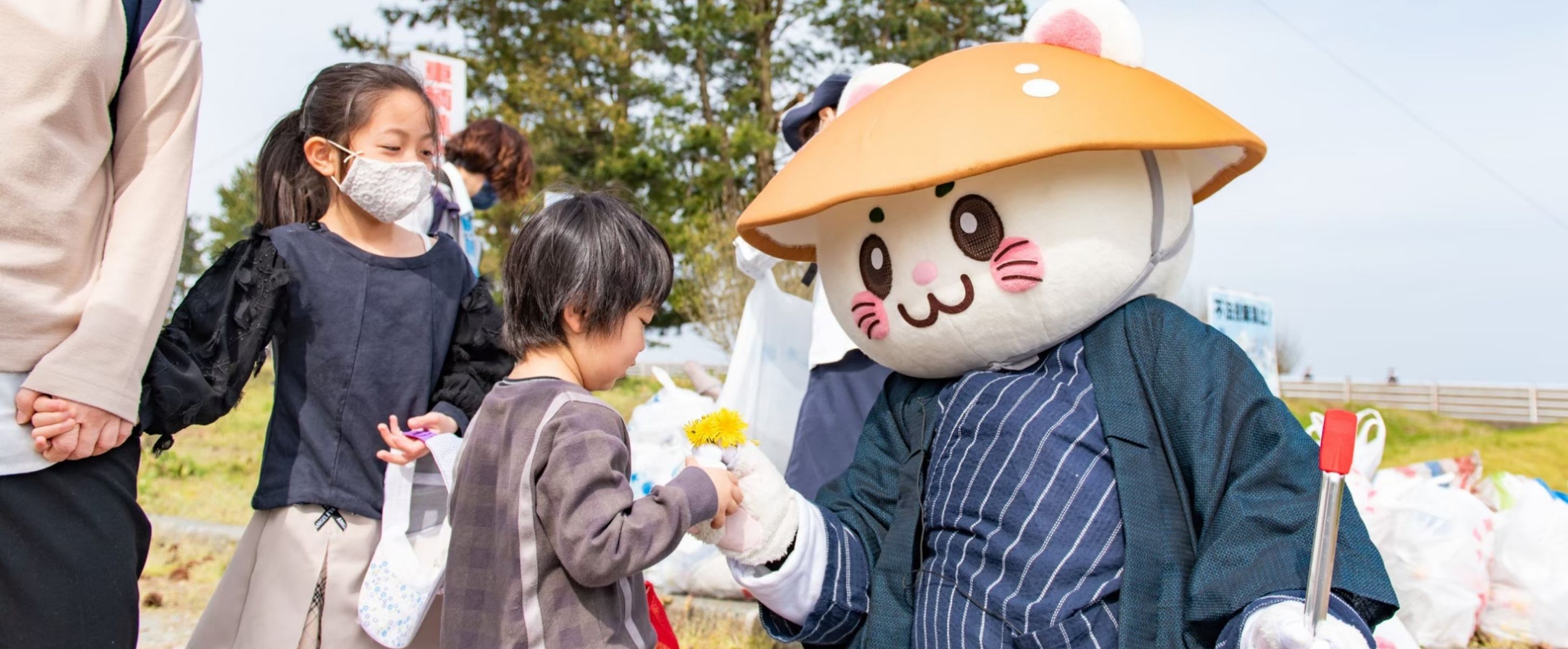 清掃活動の会場で子どもにタンポポを手渡すばいにゃこさん