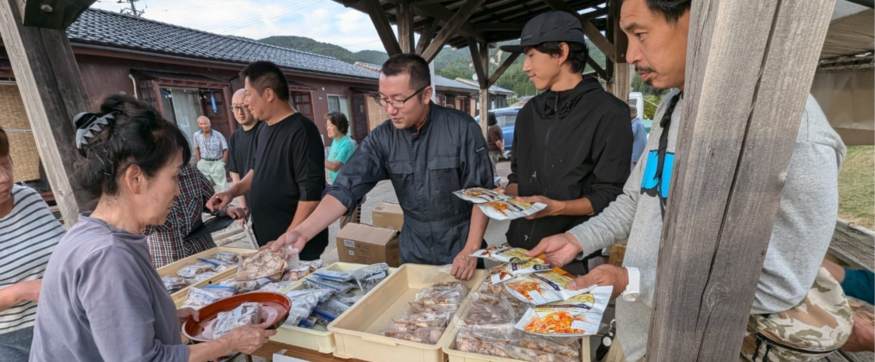 屋外の配布場で食品を手渡すメンバーと受け取る住民